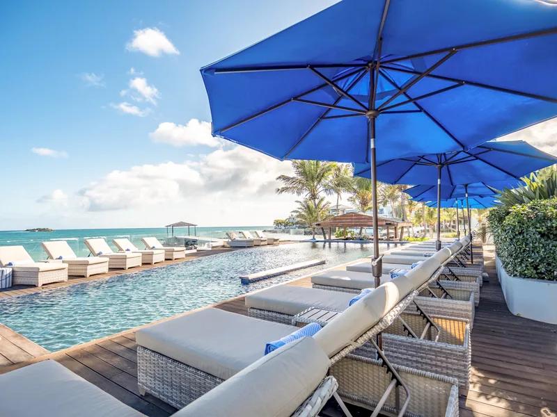 Blue parasols and day beds along a pool that runs down toward the sea