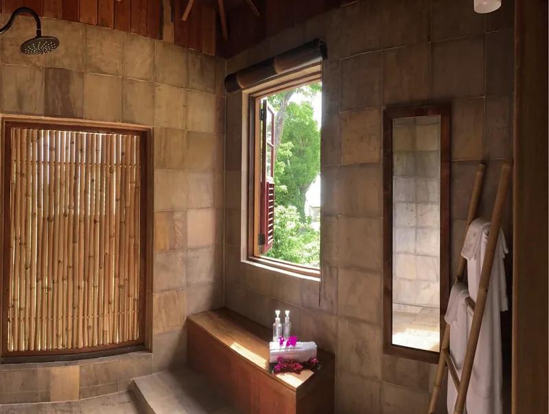 A stone-walled bathroom with a rain shower, bamboo screen and a timber ladder