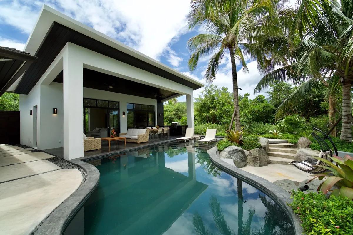 A modern white villa at Christophe Harbour, its covered terrace opening onto a long pool edged with palms and tropical planting
