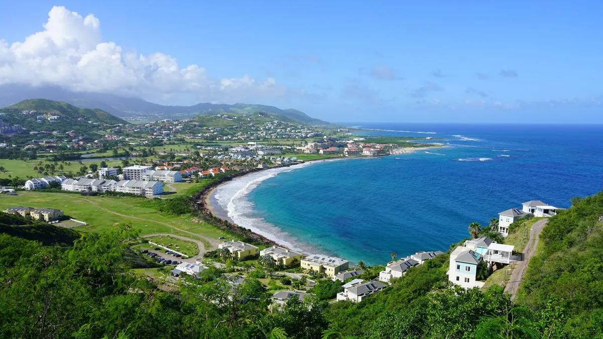 A curving bay on St Kitts seen from the ridge above, low villas scattered across the green slopes