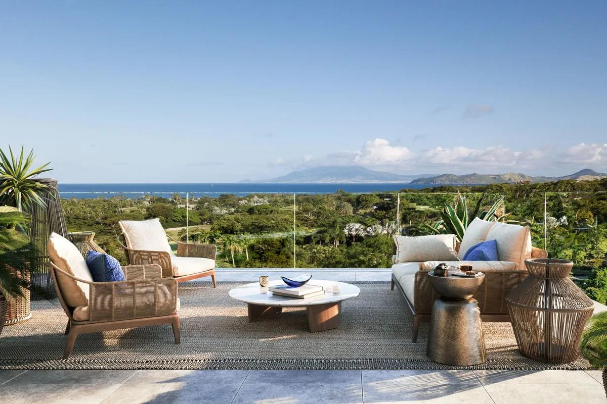 A furnished terrace looking out over low green scrub to the sea, a neighbouring island on the horizon