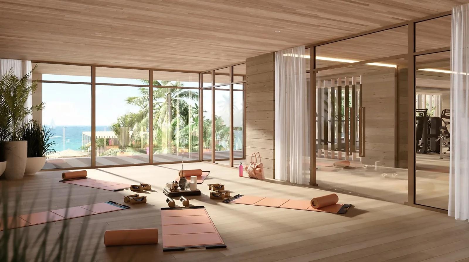 A yoga studio with mats laid out under a timber ceiling, glass walls open to the sea