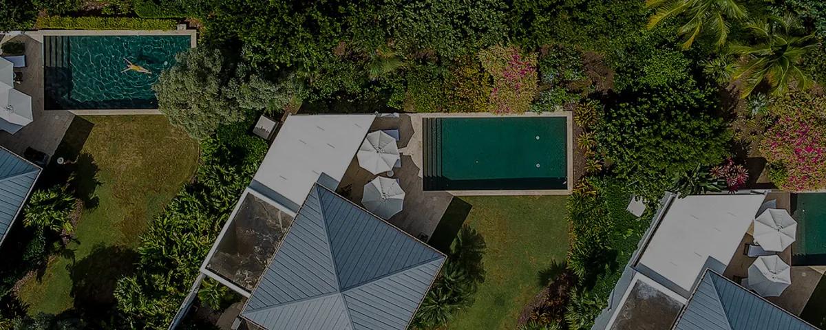 Villa roofs and two green plunge pools seen from directly above, set in dense garden